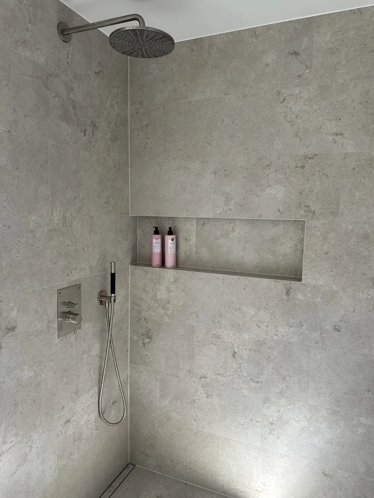 Duschvägg i granitkeramik med kalkstenslook, takdusch och infälld nisch