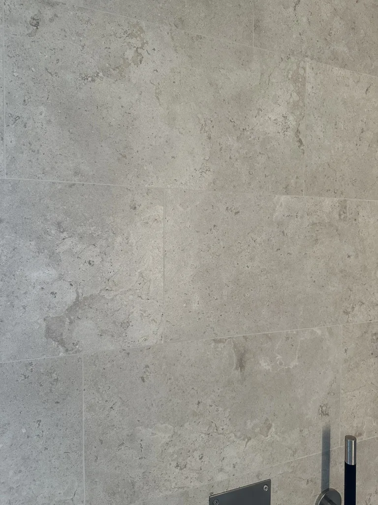 Storformats-granitkeramik med kalkstensådring och mjukt färgspel på badrumsvägg.