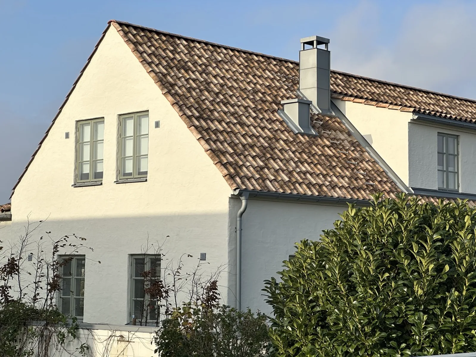 Detaljbild på tegeltak vid gavel och skorsten på vit putsad villa
