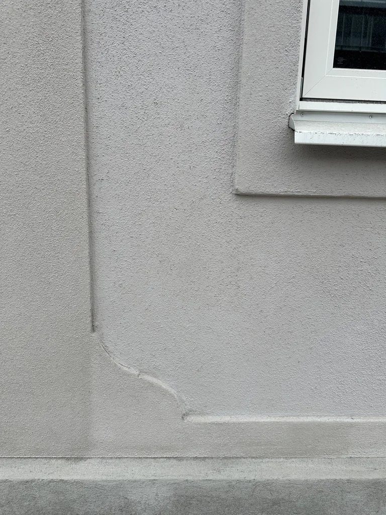Närbild på putsad fasad med sprickbildning vid fönster, exempel på renoveringsbehov.